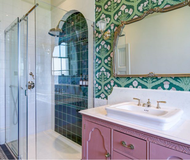 The bathroom of the Wedding Suite featuring a shower with dark green tile and a pink vanity.