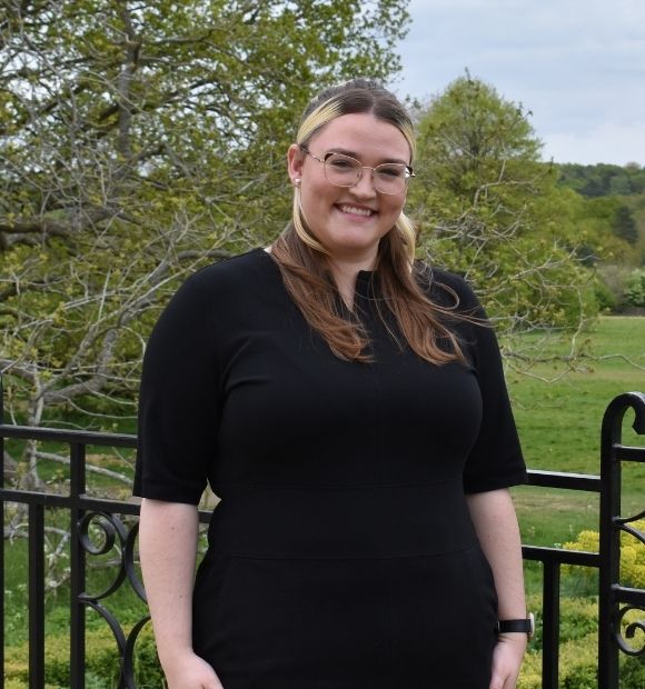 Courtney, a woman with long brunette and blonde hair, smiling while standing on the East Terrace. 