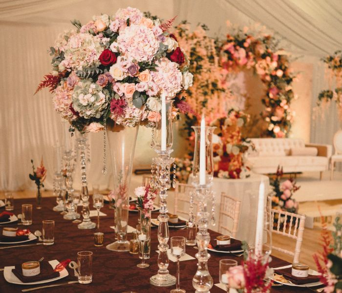 a long, rectangular table set for dinner with wine glasses and pink floral centrepieces. 