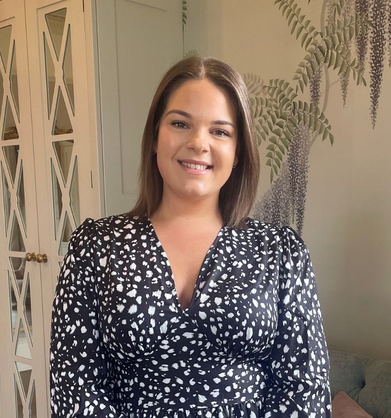 A woman with shoulder-length brunette hair and a black and white dress smiling at the camera. 