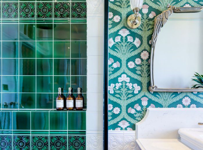 The bathroom of the Wedding Suite featuring a shower with dark green tile and pink floral wall paper. 