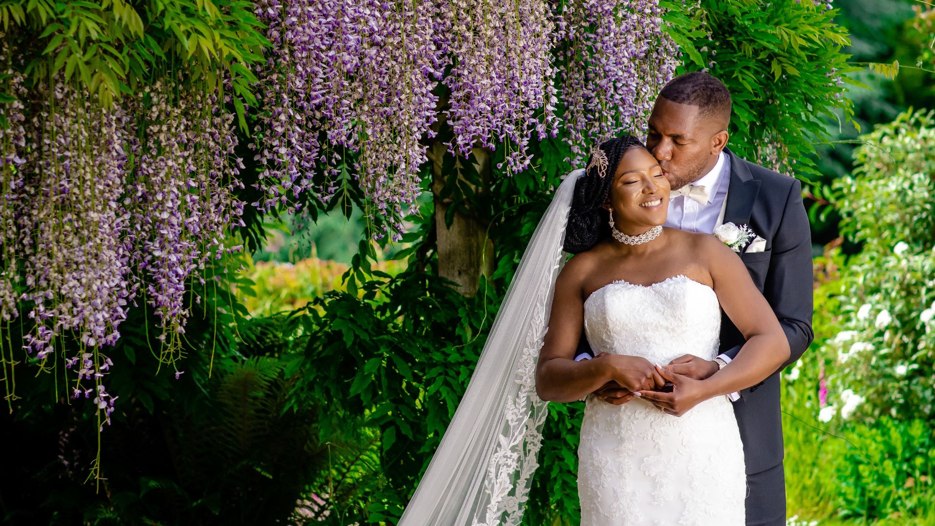 A couple smiling while standing under the wisteria