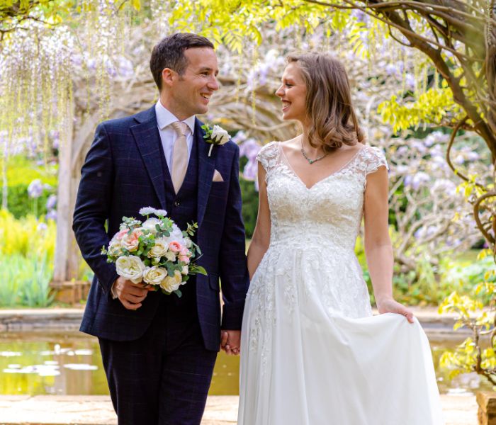 A bride and groom holing hands as they walk under the wisteria. 