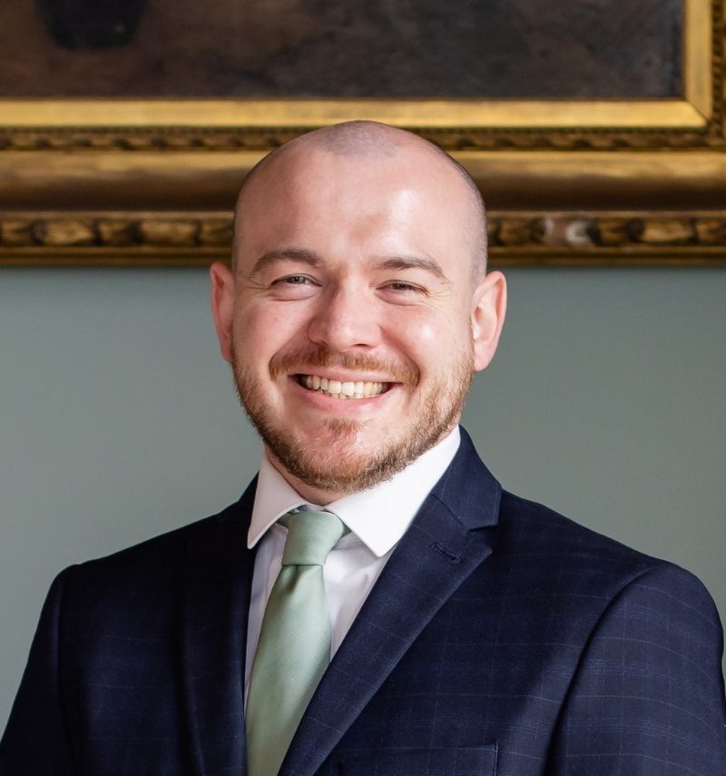 A man with a dark blue suit smiling.