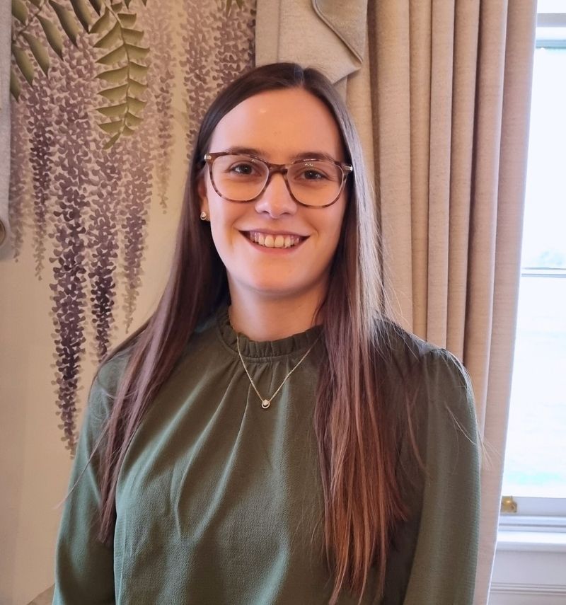 A woman with long brunette hair and glasses smiling at the camera. 