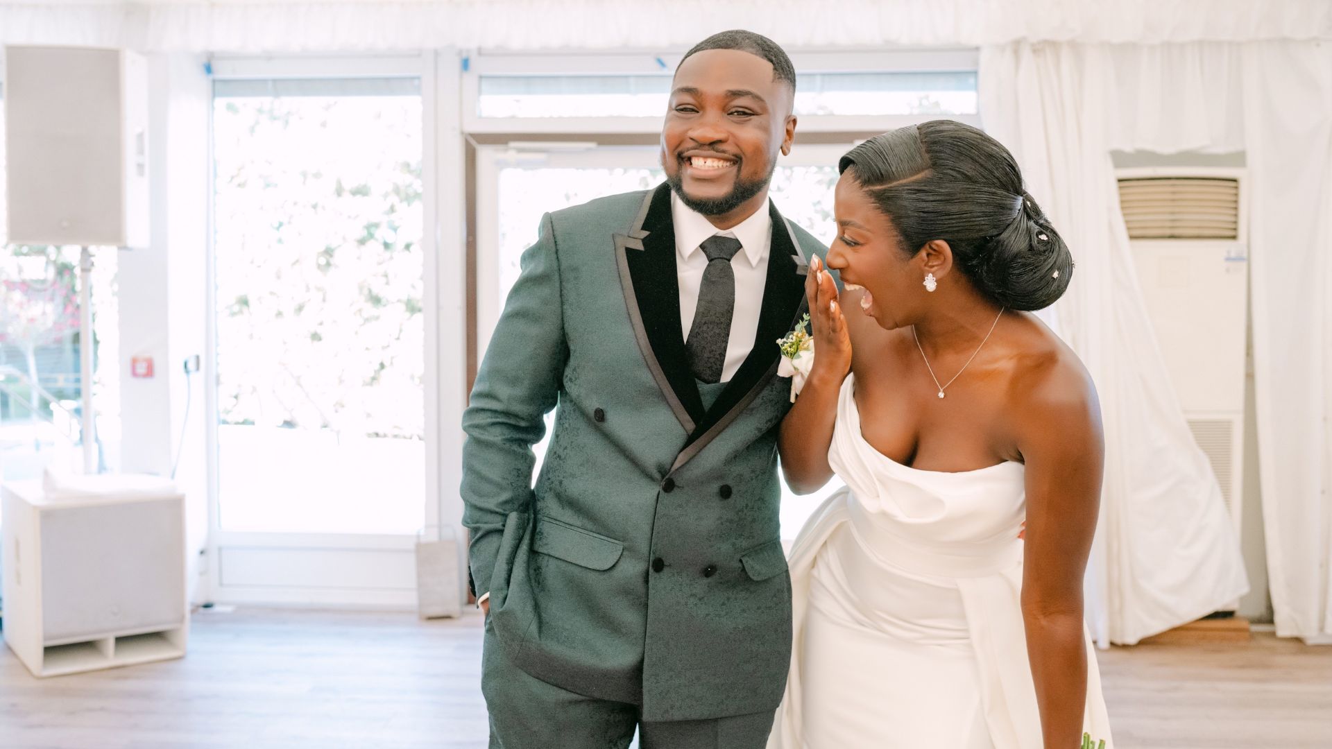 Wedding couple walking through a bright interior space, with one person holding a bouquet and both dressed in formal wedding attire.