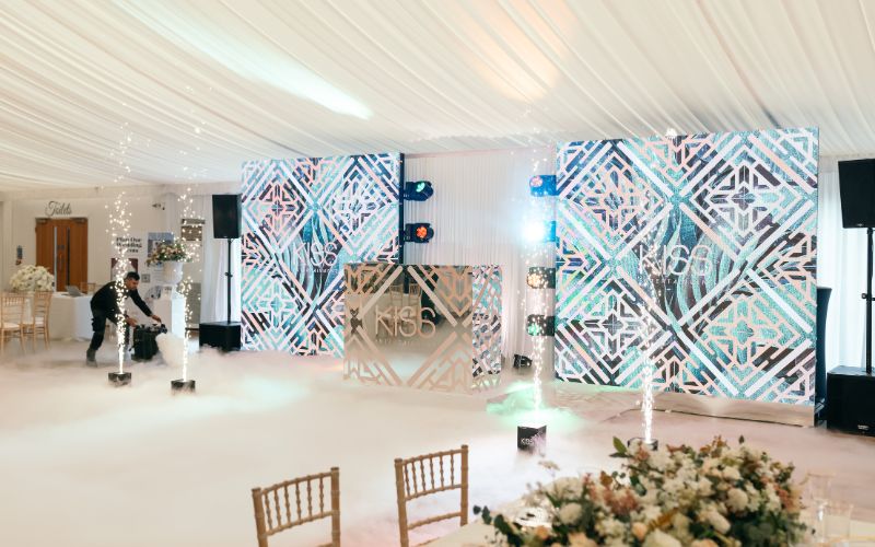 A dance floor and DJ booth decorated with silver and blue with sparklers and fog.