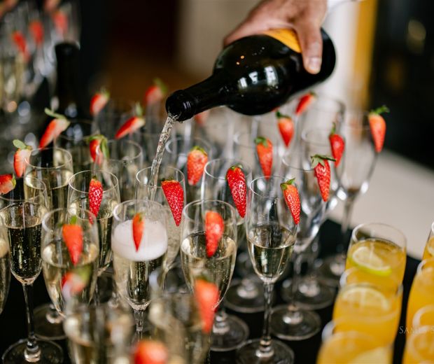 Prosecco being poured into flutes with a garnish of fresh strawberries.